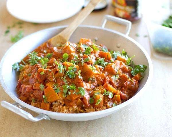 Squash coconut curry in a skillet with a wooden spoon.