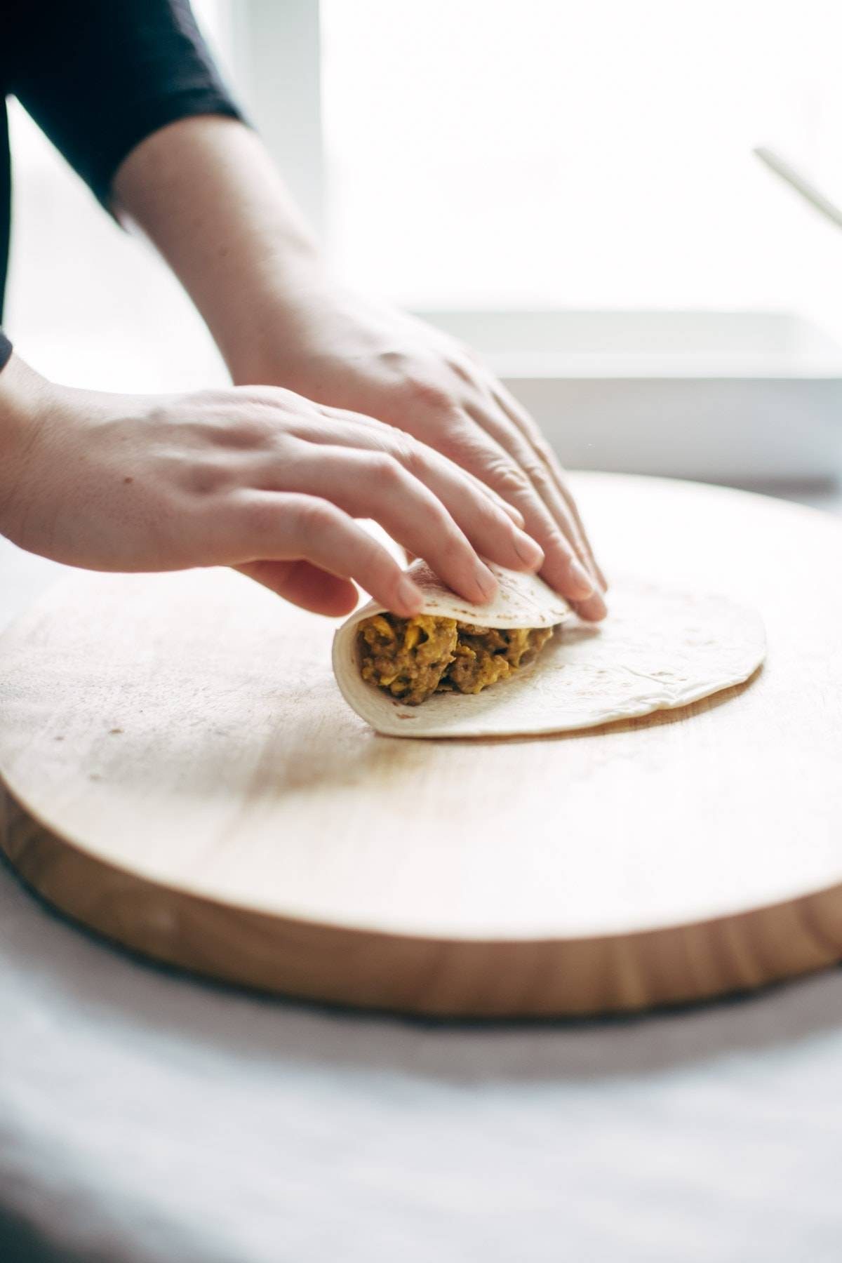 person rolling a breakfast enchilada on a wooden surface