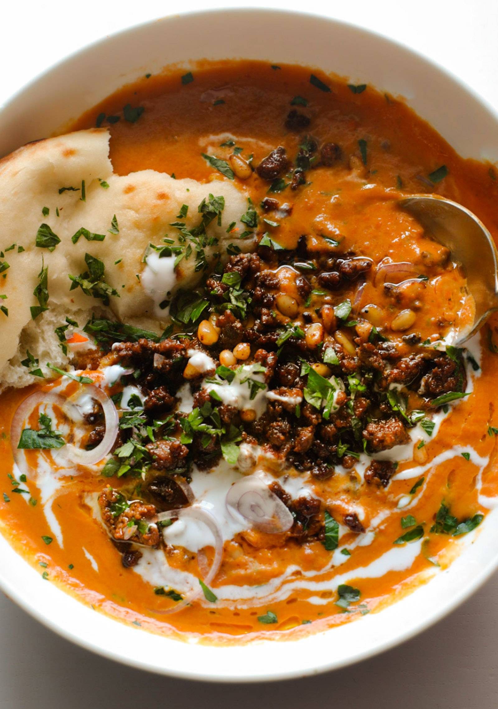 Carrot soup in a bowl topped with crispy ground beef, yogurt, and naan.