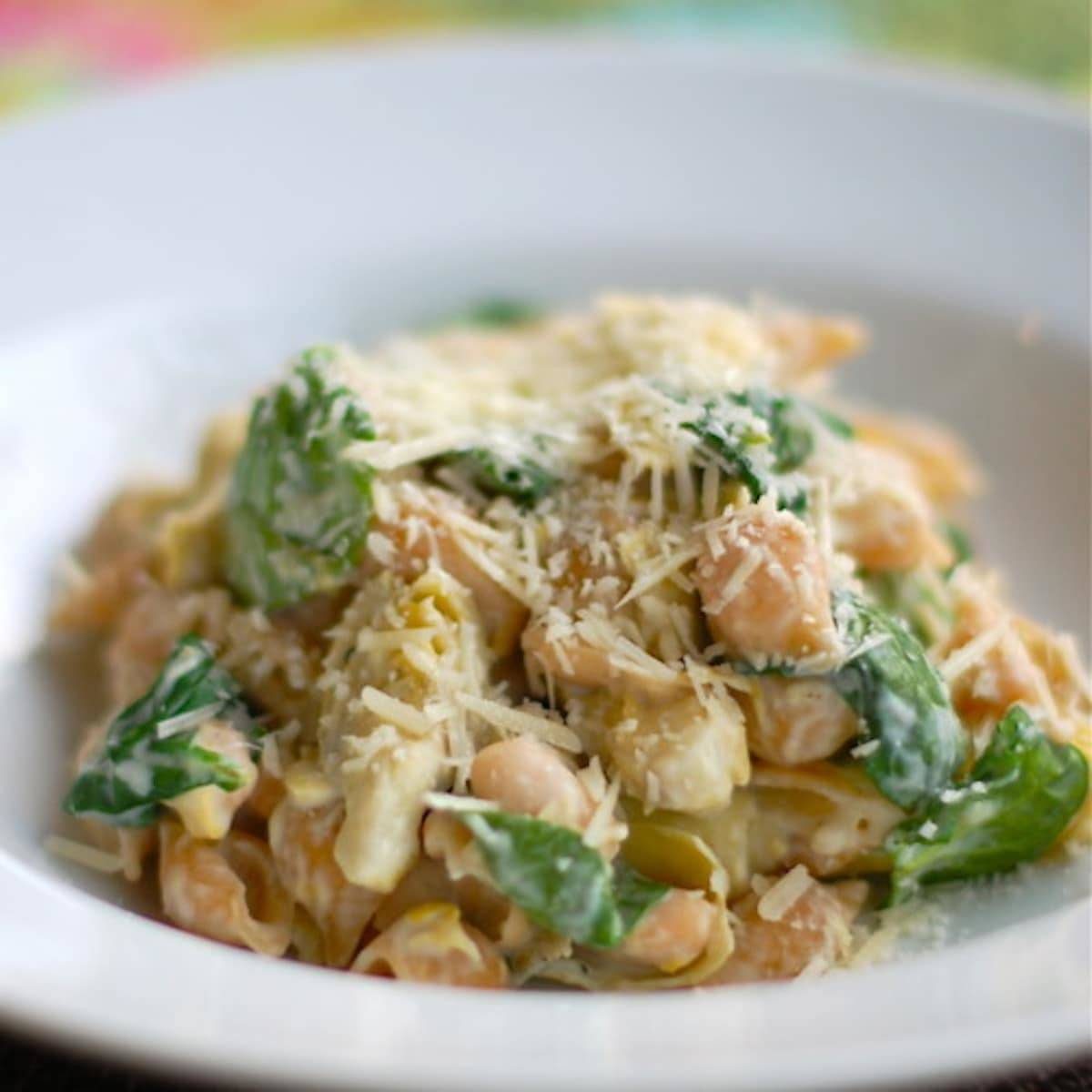 Spinach artichoke pasta in a white bowl.