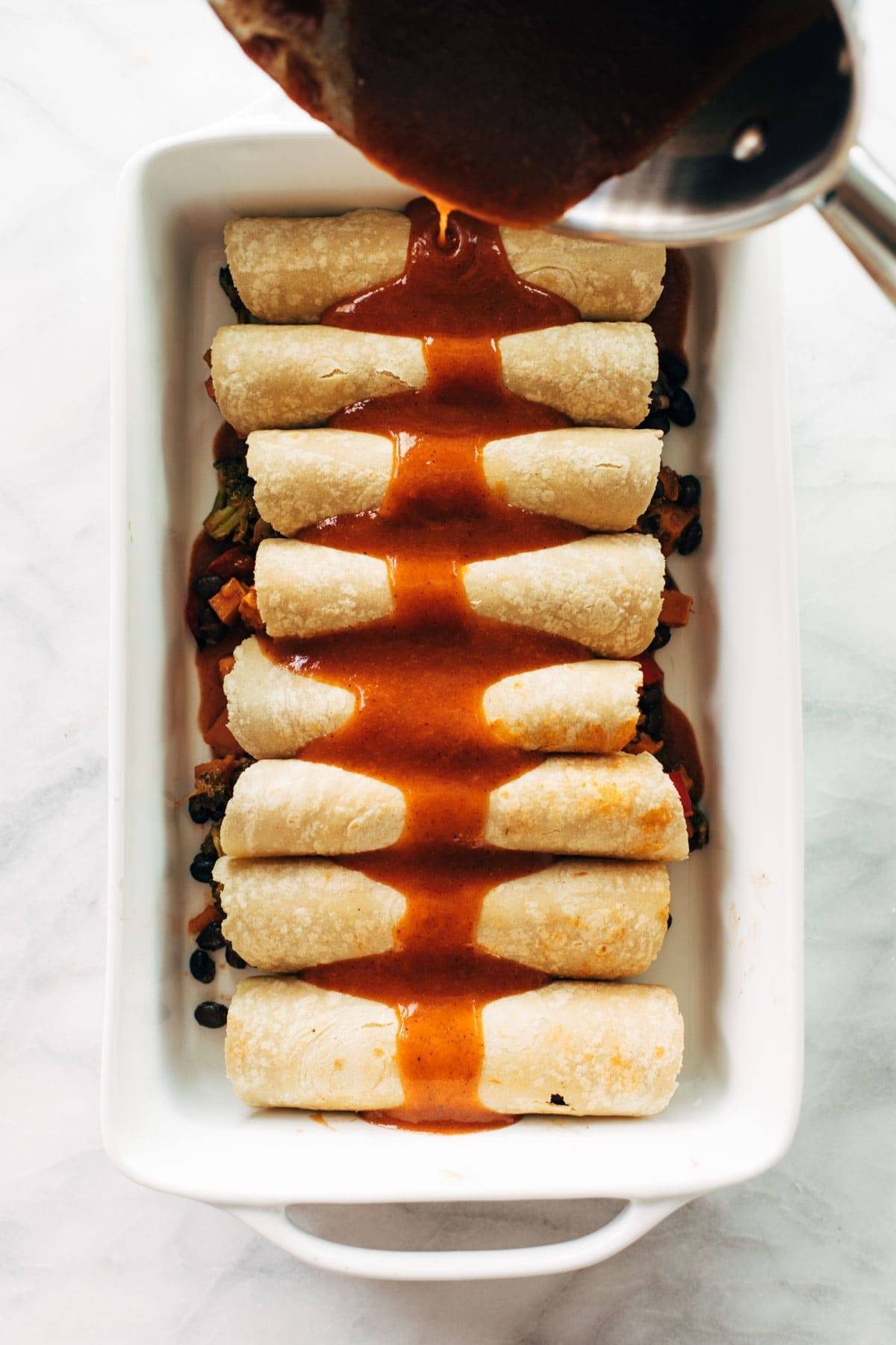 Pouring sauce on veggie enchiladas.