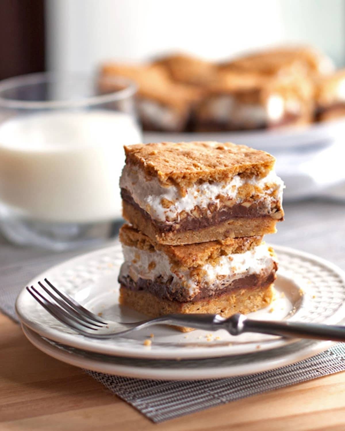 S'mores bars layered in between marshmallow fluff, chocolate, and a graham cookie base on a plate with a fork.